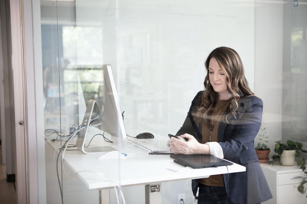 Employee stands at desk using her mobile phone to communicate